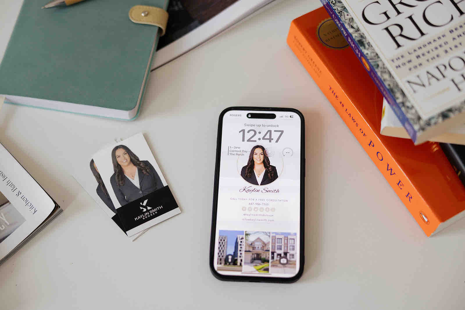 A business card, notebook and stack of business books on a desk.