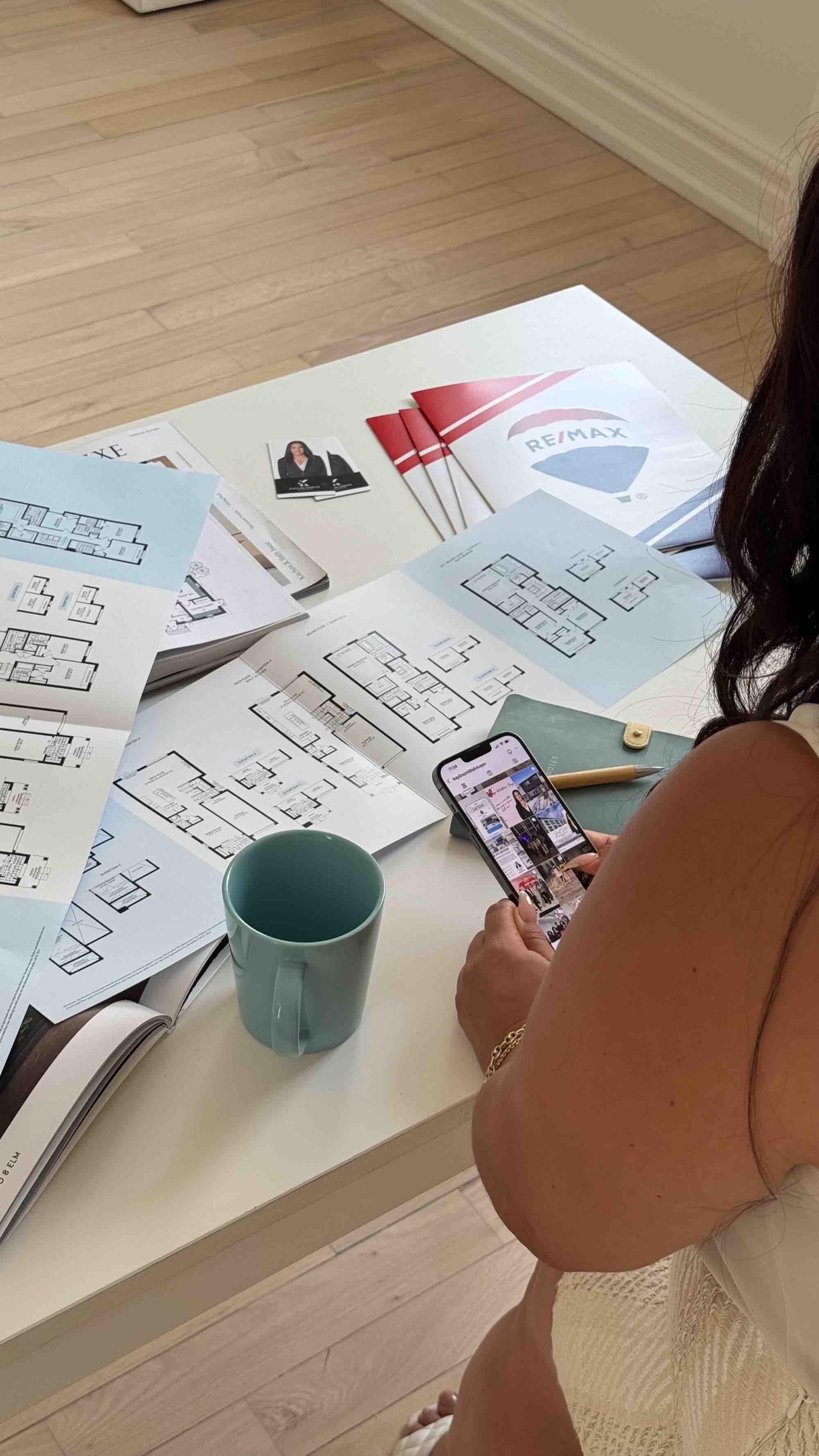 Kaylin Smith at a desk covered in floor plans, RE/MAX marketing material beside her.