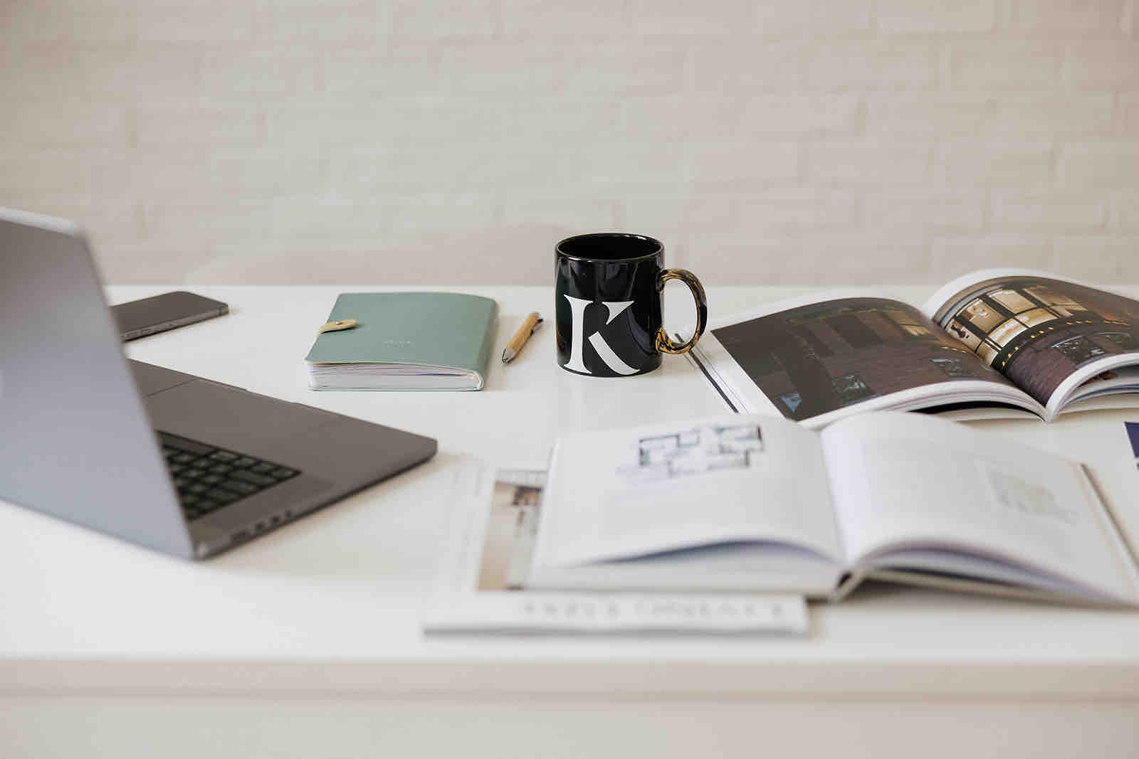 A desk with a laptop, notebook and architecture books, and a mug marked with a K.